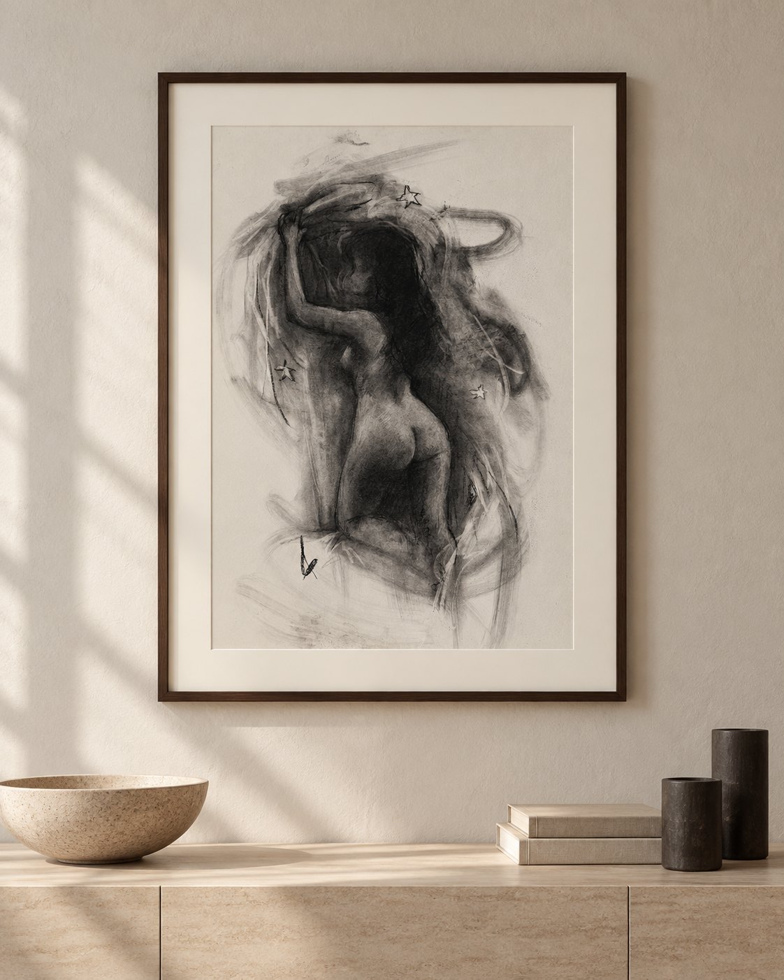 Charcoal drawing of a nude woman seen from behind, one arm raised into dark swirling strokes and small stars, framed in dark wood above a stone sideboard in warm sunlight