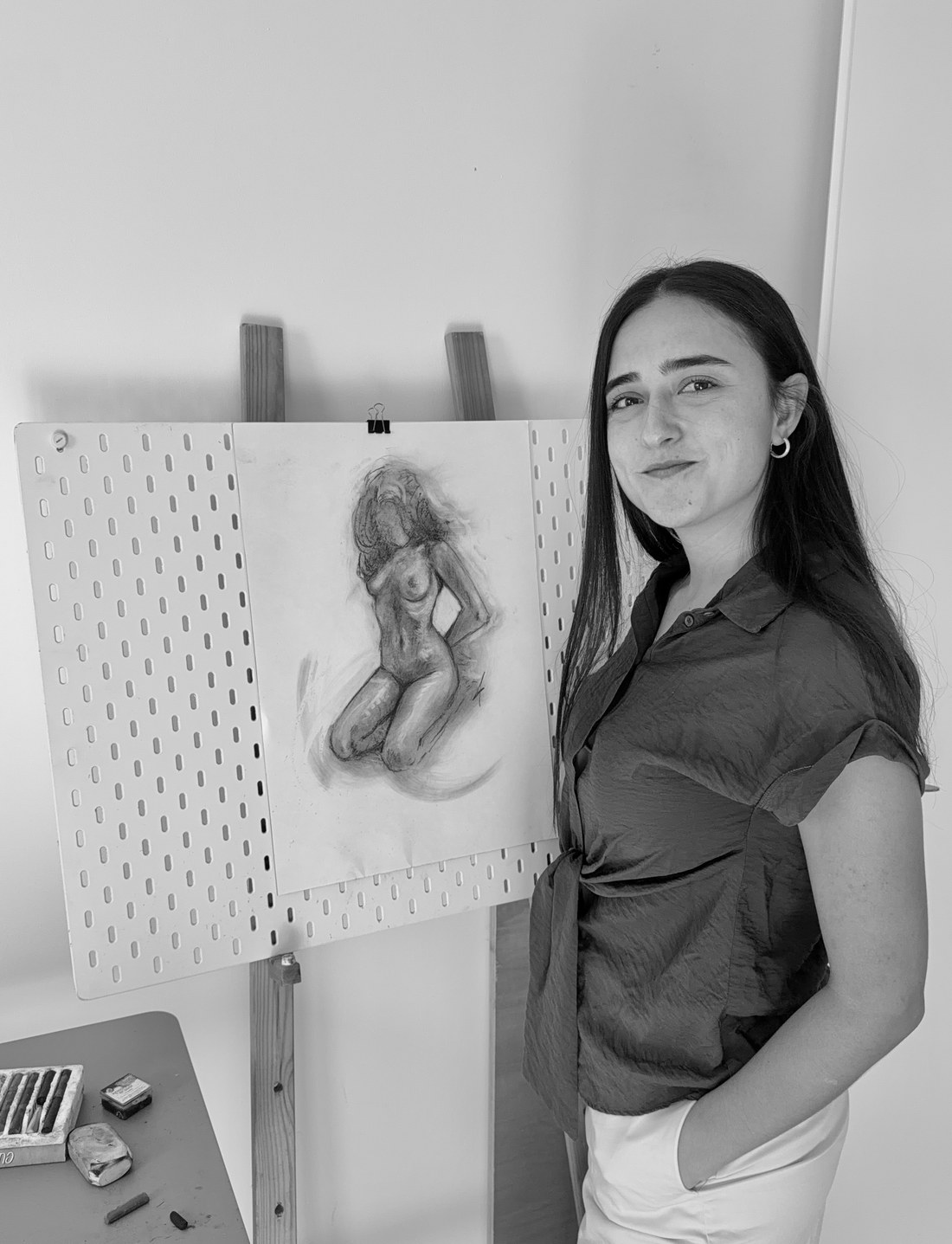 Nicol standing beside an easel with a charcoal figure drawing in progress