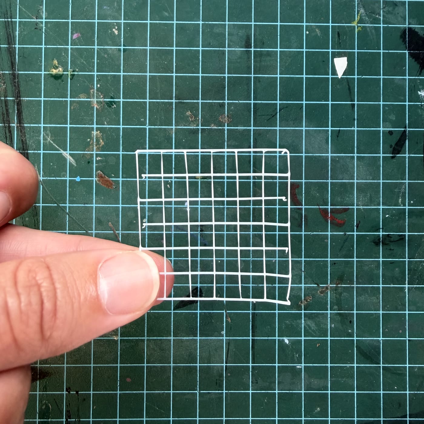 First physical test print of the woven grid pattern, a small plastic mesh held between two fingers on a cutting mat