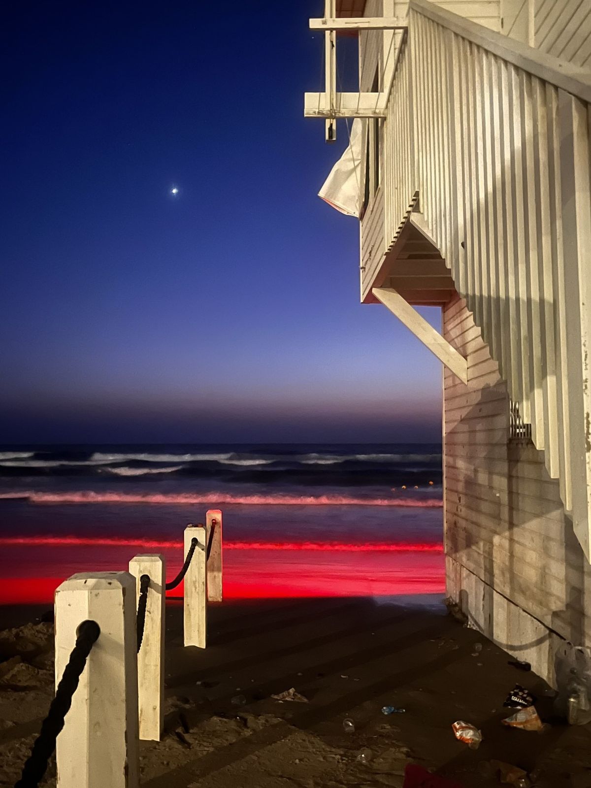 Open series: Red Neon Sign — a beach lifeguard tower at dusk with sand lit red by a neon bathing sign