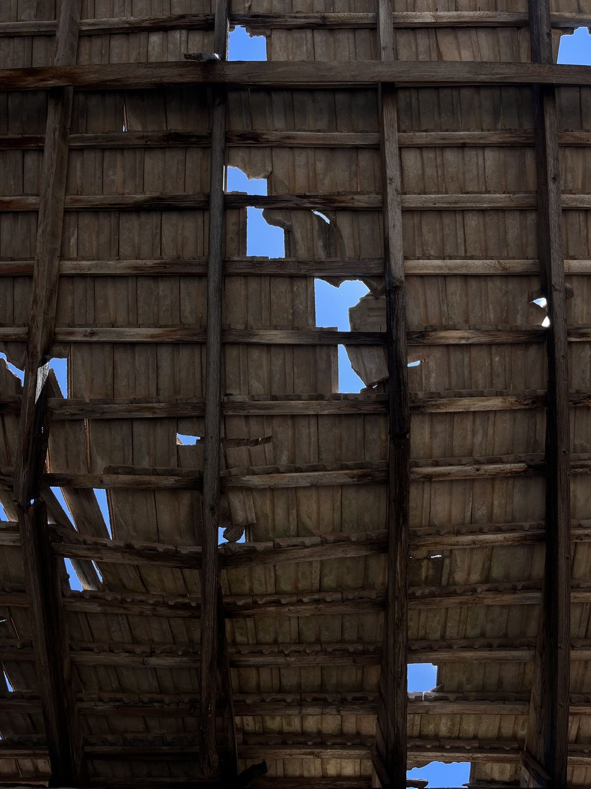 Close view of a broken tiled roof with jagged holes letting in blue sky