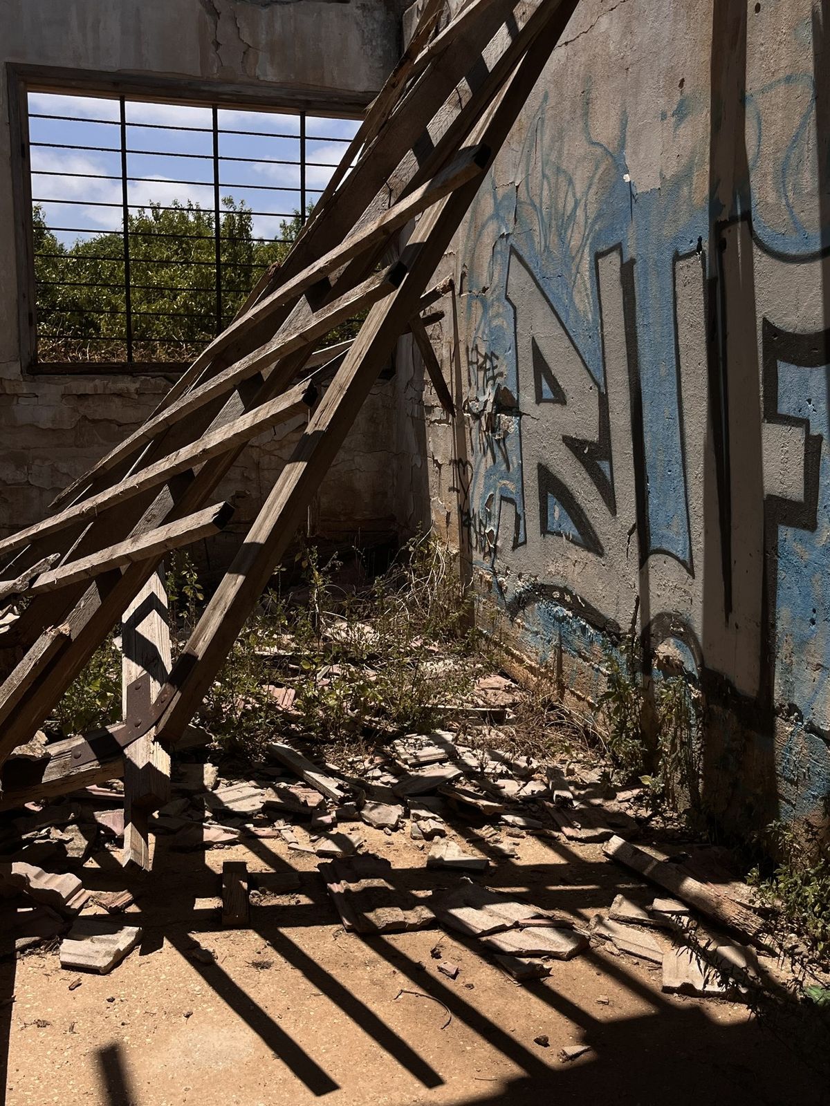 A collapsed wooden roof truss leaning against a graffiti-covered concrete wall