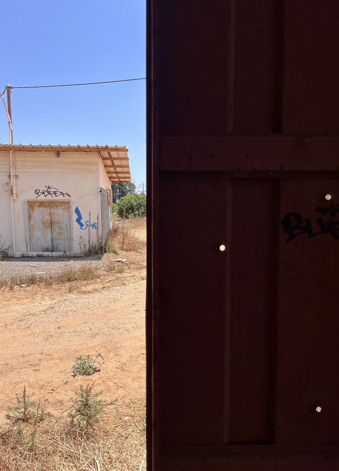 Exterior view of the abandoned building's weathered facade and rusted shutter door, seen through a doorway