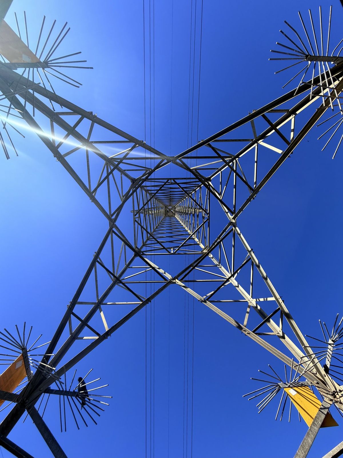 Open series: Power Poles — looking straight up through a steel transmission tower against a blue sky