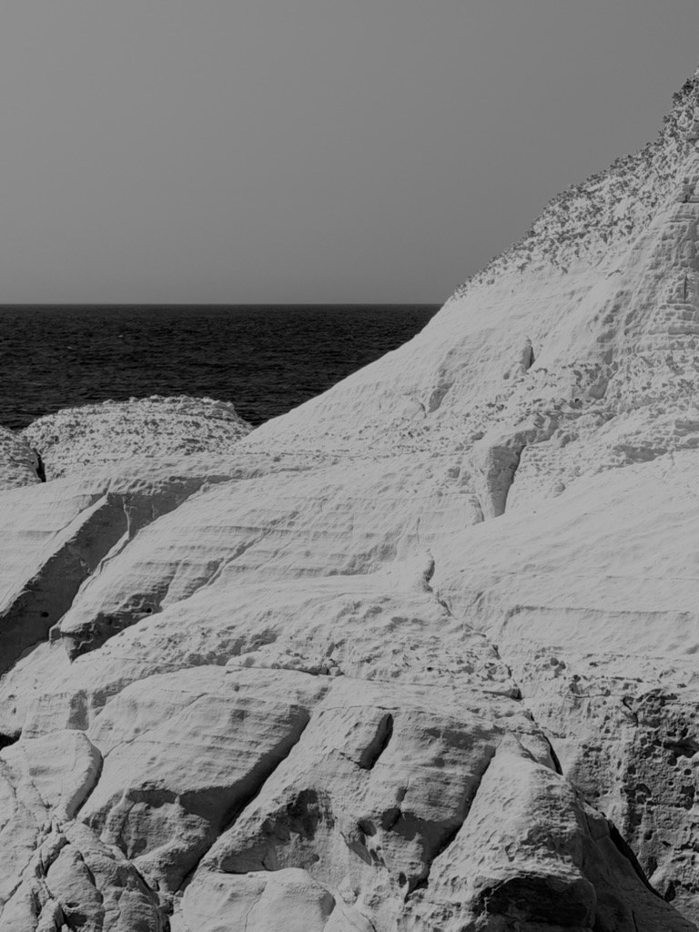 White chalk rock of the Rosh HaNikra cliffs, smooth and cracked, sloping down toward a dark sea under a grey sky