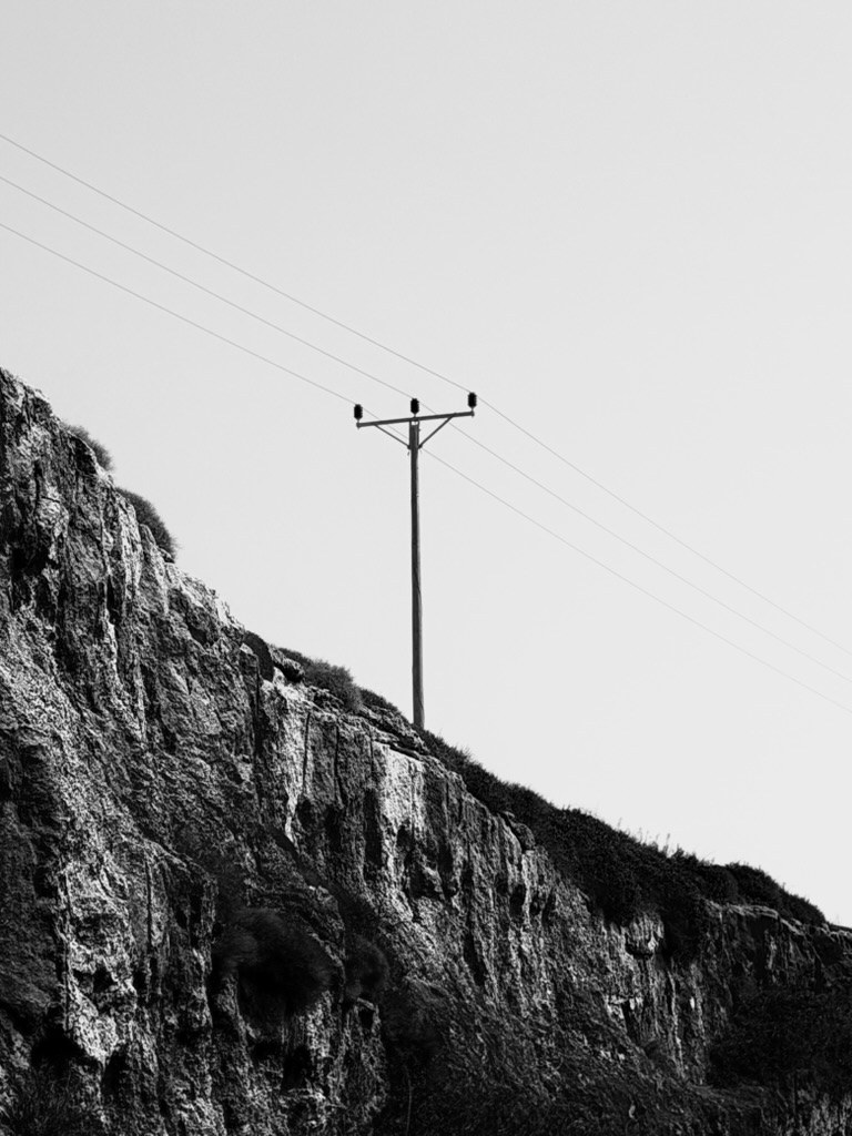 A wooden power pole and its wires on the edge of a jagged rock cliff against a pale sky