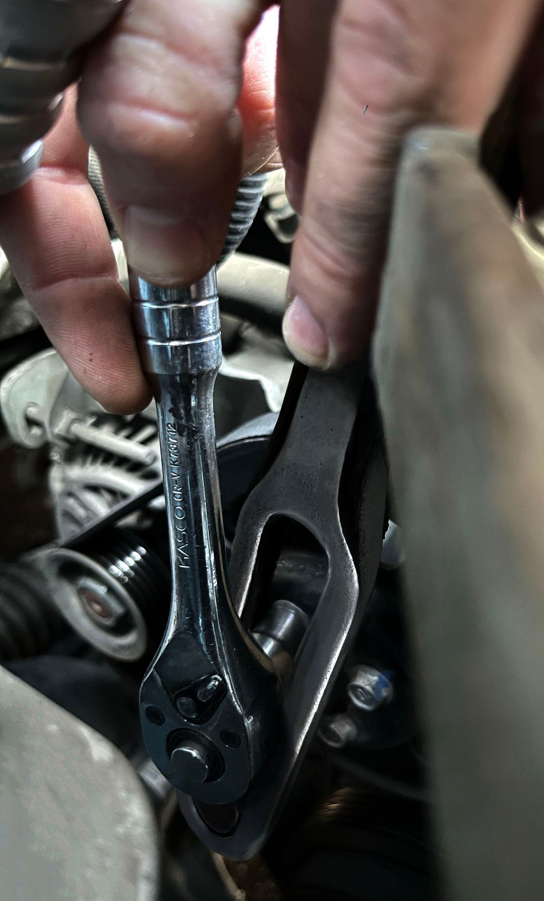 The pulley tool in use in an engine bay, steadying the water pump pulley while a ratchet loosens a bolt